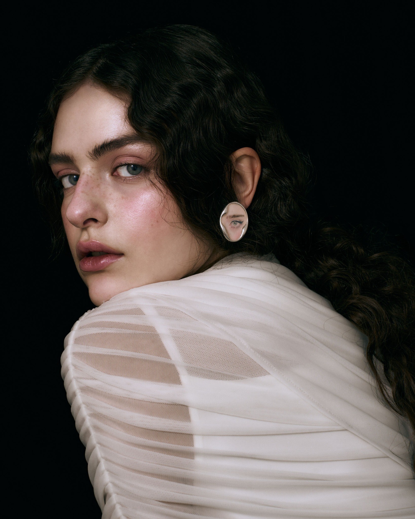 Eye portrait earring worn with sheer ivory fabric