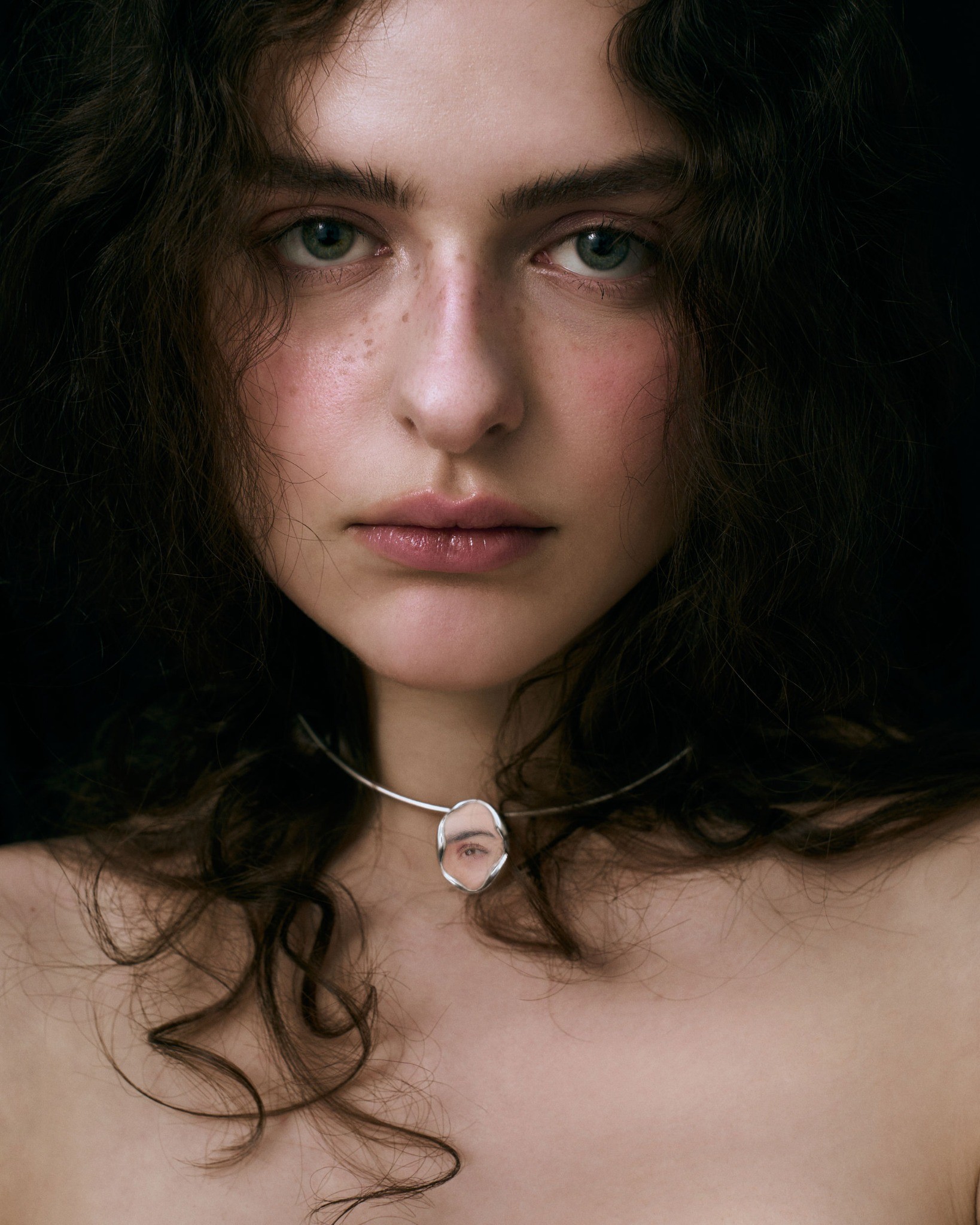 Close portrait showing a miniature eye pendant at the neck