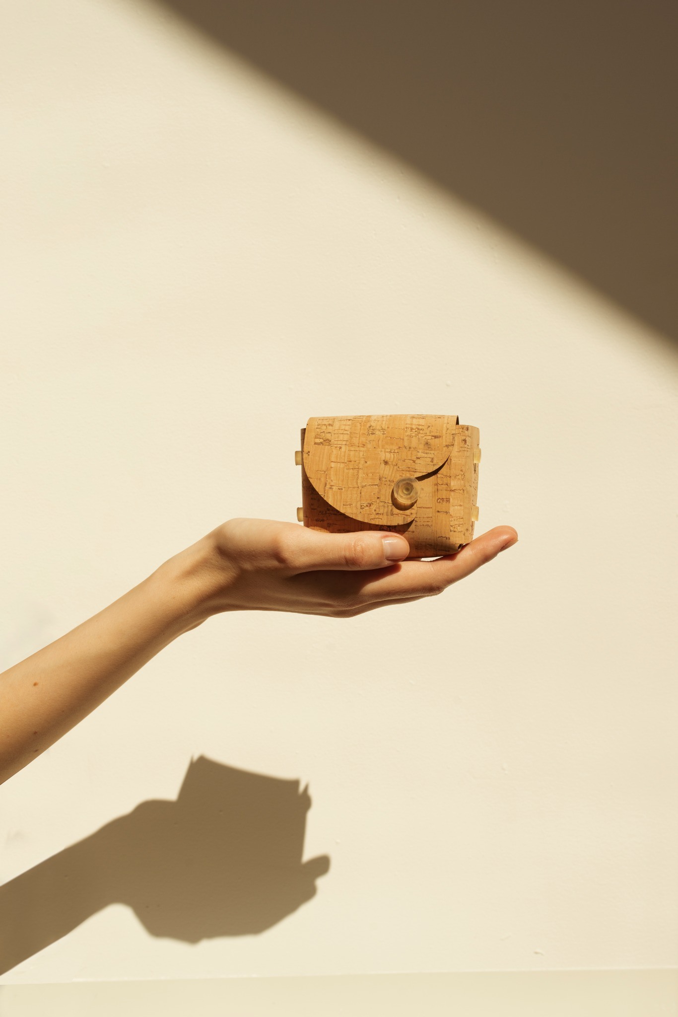 Folded cork pouch held in a hand with a sharp shadow
