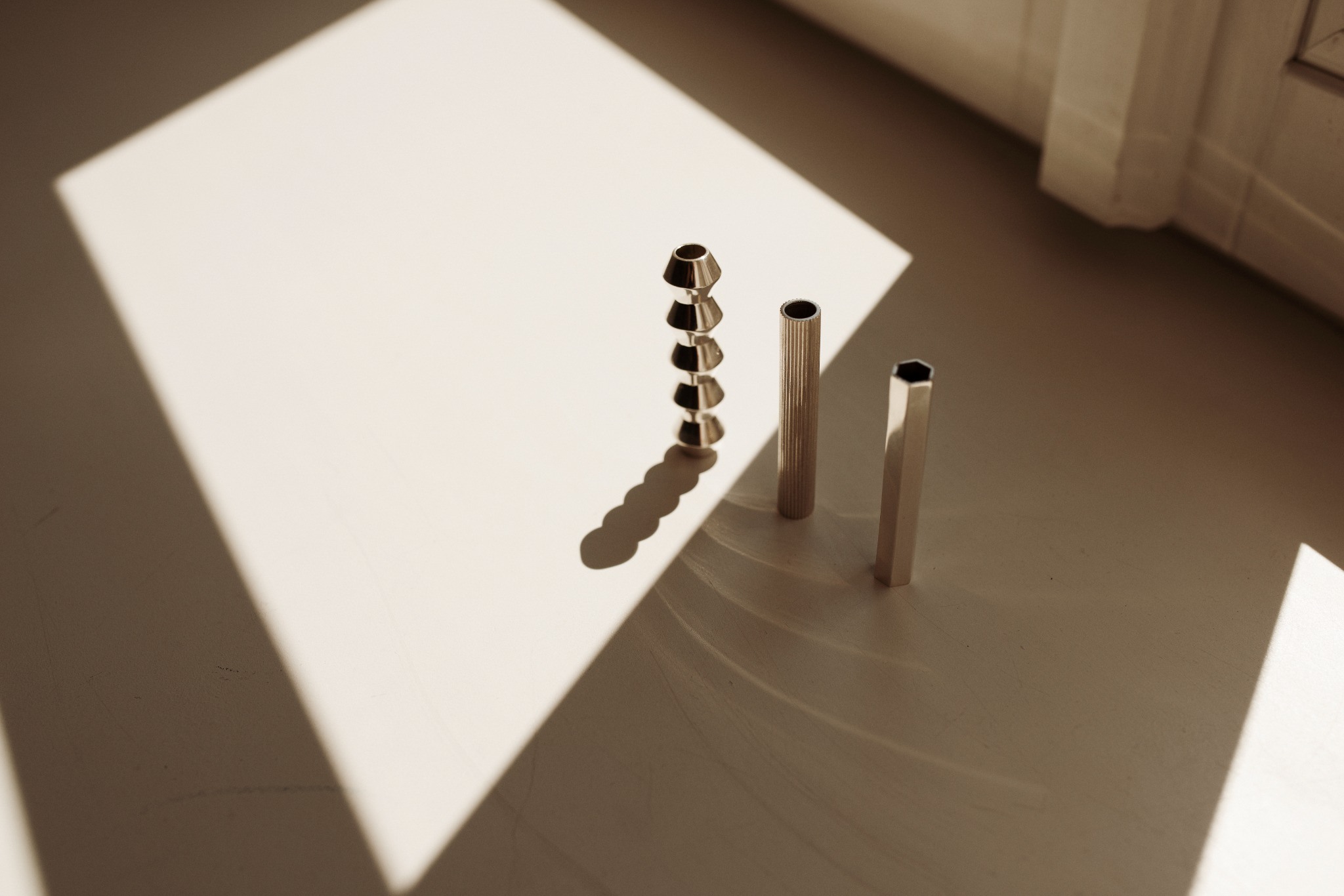 Three silver jewelry elements in geometric sunlight